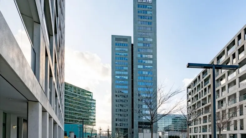 Moderne Hochhäuser und Bürogebäude in einer städtischen Umgebung mit Grünflächen und klarem Himmel.
