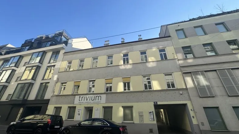Gebäudeansicht von der Straße mit gelber Fassade, vielen Fenstern und geparkten Autos davor.
