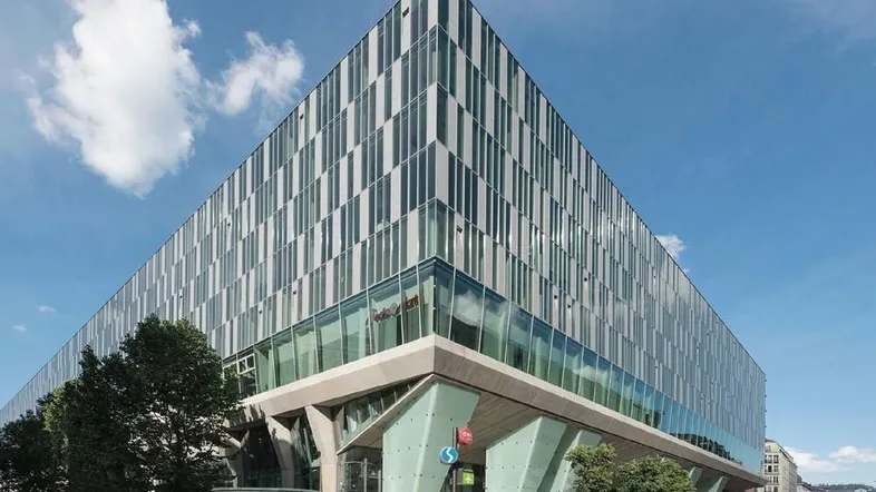 Modernes Bürogebäude mit markanter Glasfassade und vertikalen Lamellen unter blauem Himmel.