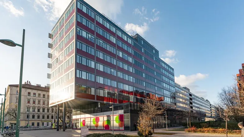 Modernes Bürogebäude mit roter Fassade und großen Glasflächen unter strahlend blauem Himmel.