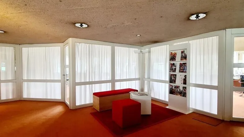 Empfangsbereich mit orangefarbenem Teppichboden, weißen Trennwänden und modernen Sitzgelegenheiten unter einer hohen Decke.