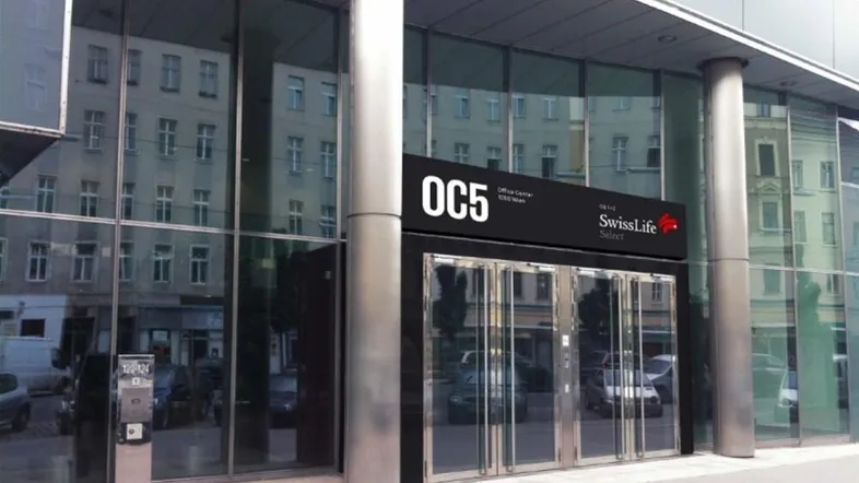 Moderner Eingangsbereich eines Bürogebäudes mit großer Glasfassade und Säulen.