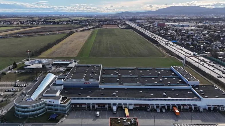 Luftaufnahme eines großen Industriegebäudes mit angrenzender Autobahn, Feldern und weitläufiger Landschaft.