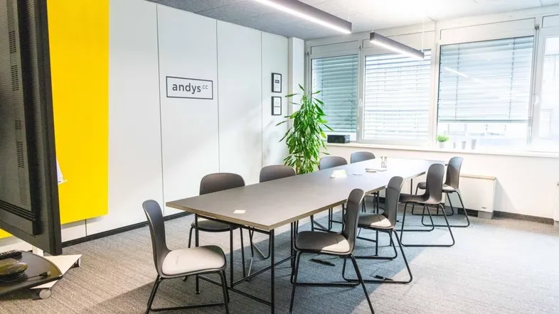Moderner Konferenzraum mit großem Tisch, bequemen Stühlen und viel Tageslicht durch große Fenster.