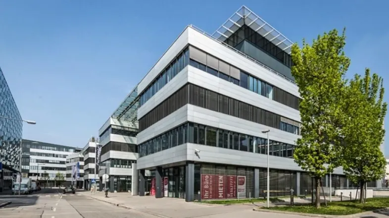Modernes Bürogebäude mit Glasfassade und Metallverkleidung unter blauem Himmel.