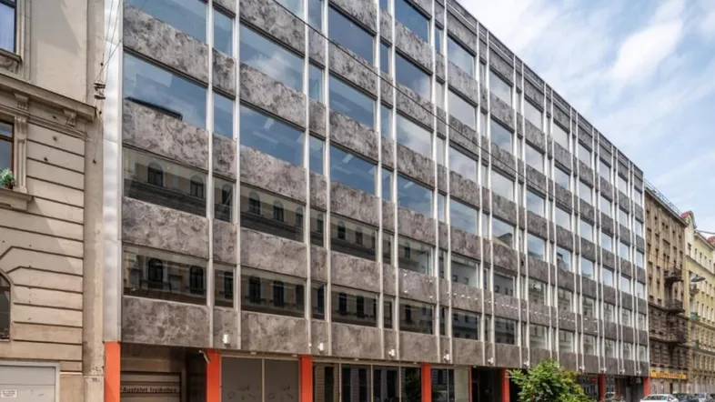 Modernes Bürogebäude mit großer Glasfassade und Betonverkleidung in städtischer Umgebung.