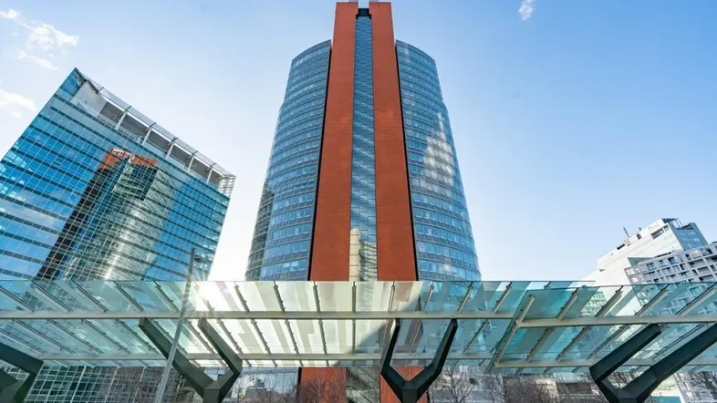 Moderne Hochhäuser mit Glasfassaden und einem markanten roten Turm unter blauem Himmel.