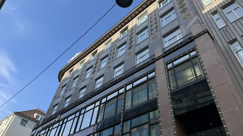 Fassade eines mehrstöckigen Gebäudes mit vielen Fenstern und architektonischen Details unter blauem Himmel.