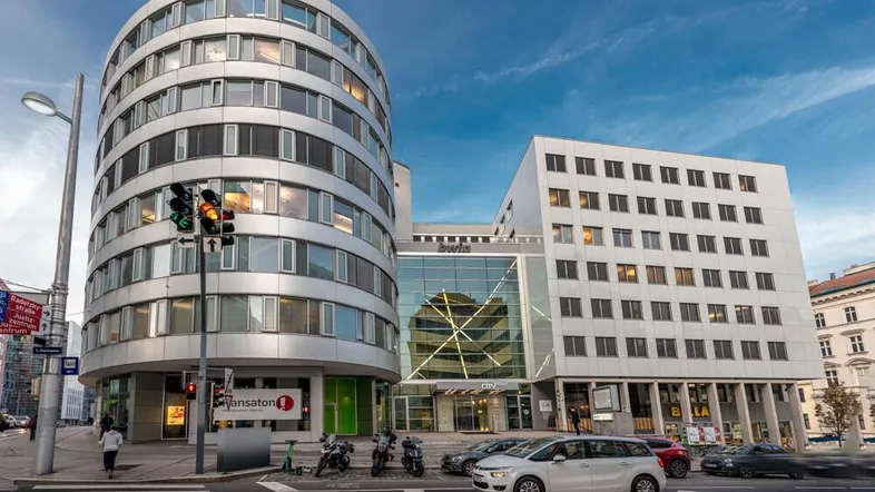 Moderne Bürogebäude an einer belebten Straßenkreuzung mit markanter Architektur und vielen Fenstern.