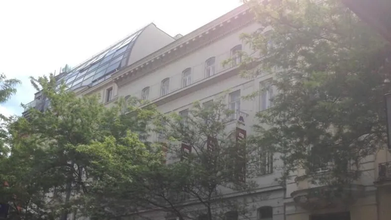 Fassade eines klassischen Gebäudes mit Geschäften im Erdgeschoss und Bäumen davor.
