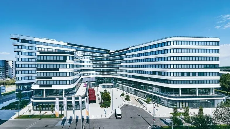 Moderne Bürogebäude-Fassade mit geschwungenen Linien und großen Fensterfronten unter blauem Himmel.