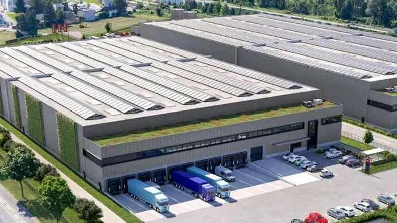 Luftaufnahme von zwei modernen Lagerhallen mit Gründächern und Solaranlagen, umgeben von Parkplätzen und Laderampen.
