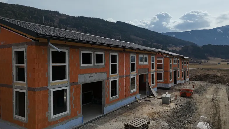 Reihenhäuser im Rohbau mit sichtbaren Ziegelwänden und Fenstereinbauten in ländlicher Umgebung.
