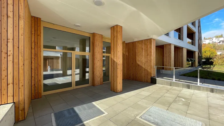 Moderner Eingangsbereich eines neuen Gebäudes mit Holzverkleidung und großen Glasfronten.