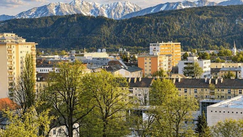 Panoramablick über die Stadt mit schneebedeckten Bergen im Hintergrund unter einem blauen Himmel.