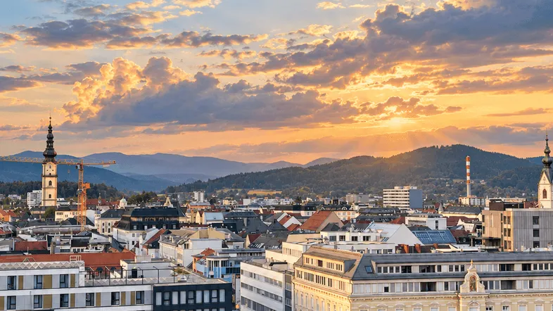 Panoramablick über die Stadt bei Sonnenuntergang mit Bergen im Hintergrund und dramatischen Wolken.