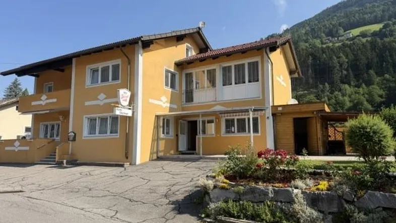 Gelbes Gebäude mit traditioneller Architektur, umgeben von Bergen und grüner Landschaft unter blauem Himmel.