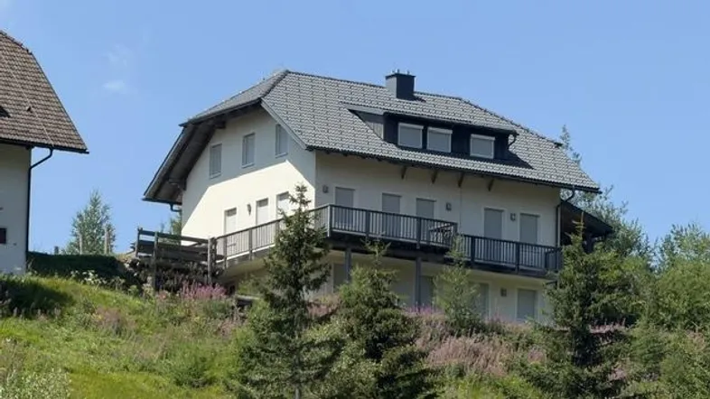 Ein charmantes Haus mit mehreren Balkonen, eingebettet in eine grüne Hügellandschaft unter blauem Himmel.
