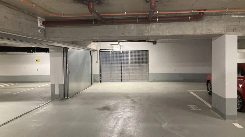 Tiefgarage mit Betonwänden, sichtbaren Rohren an der Decke und einem roten Auto am Rand.
