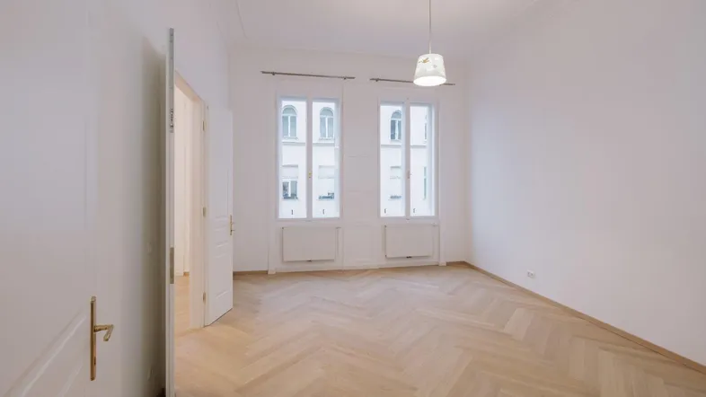 Helles, leeres Zimmer mit Fischgrätparkett und hohen Fenstern, bereit zur Einrichtung.