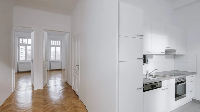Moderne Einbauküche mit weißen Schränken, integrierten Geräten und Blick in den Flur mit Fischgrätparkett.