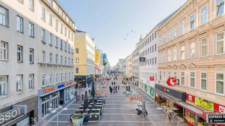 Belebte Einkaufsstraße mit historischen Gebäuden und Geschäften unter klarem Himmel.