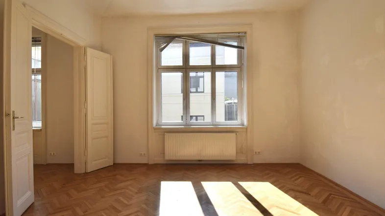 Helles Zimmer mit Fischgrätparkett und viel Tageslicht durch das große Fenster.