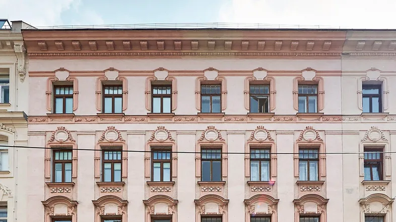 Historische Fassade eines Altbaus mit eleganten Verzierungen und großen Fenstern.