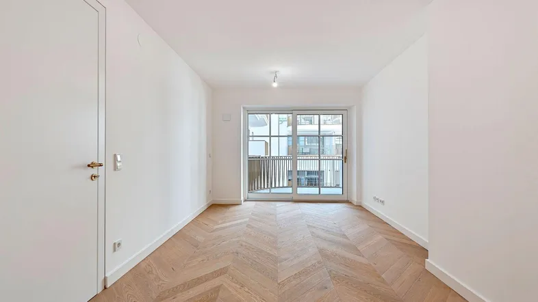 Helles Zimmer mit modernem Fischgrätparkett und Zugang zu einem Balkon.