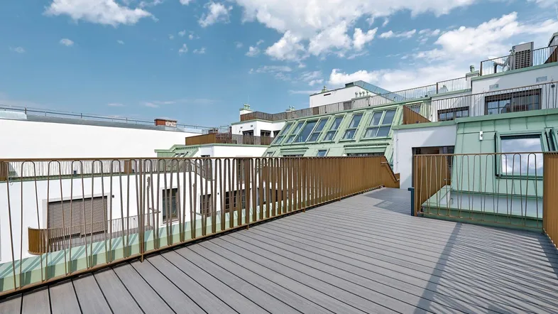 Geräumige Dachterrasse mit Holzoptik-Bodenbelag und Blick auf die umliegenden Gebäude unter blauem Himmel.