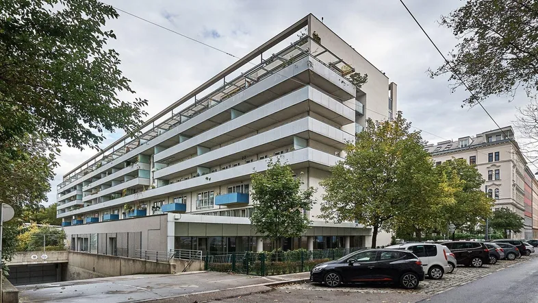 Modernes Wohngebäude mit langen Balkonen und Tiefgaragenzufahrt an einer städtischen Straße.