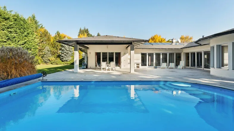 Großer Außenbereich mit Pool, überdachter Terrasse und Liegeflächen unter blauem Himmel.