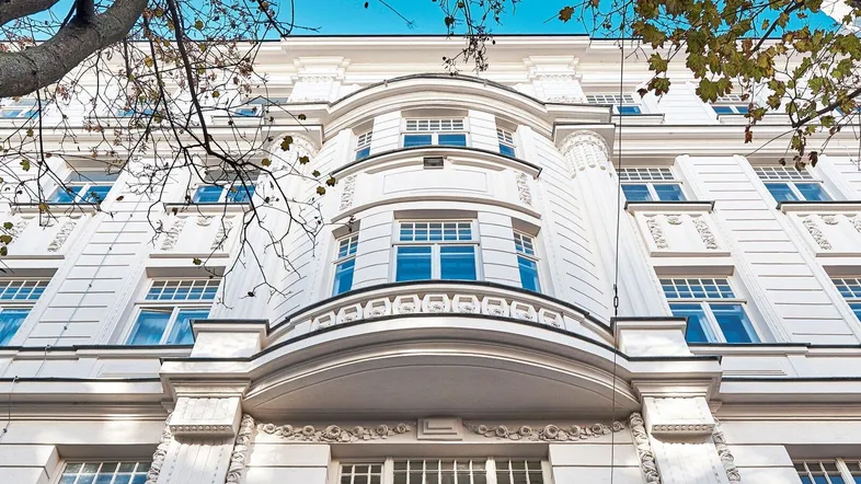 Weißes, klassisches Gebäude mit reich verzierten Fassadendetails und blauen Fenstern unter klarem Himmel.