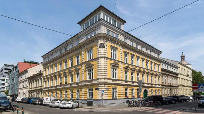 Historisches Gebäude mit gelber Fassade und moderner Dachaufstockung an einer Straßenecke.