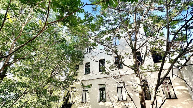 Fassade eines Wohngebäudes, umgeben von üppigem Grün und Bäumen unter blauem Himmel.