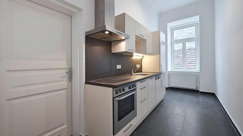 Moderne Einbauküche mit dunklen Fliesen, Dunstabzugshaube und Fenster, bereit zur Nutzung.
