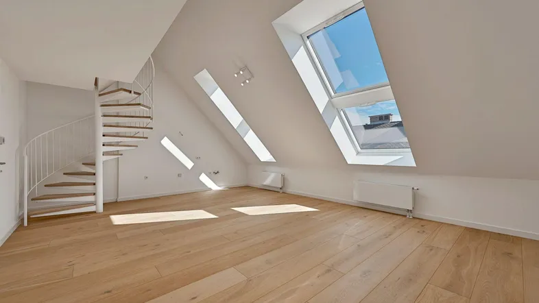 Heller Wohnraum im Dachgeschoss mit Holzfußboden, Wendeltreppe und großen Dachfenstern.