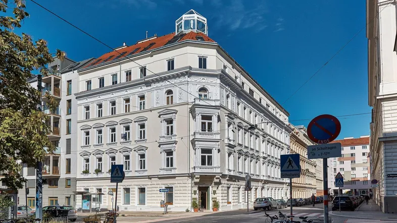 Elegantes Eckgebäude in urbaner Umgebung mit klassischer Architektur und vielen Fenstern.