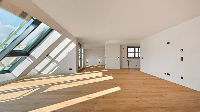 Helles, offenes Dachgeschosszimmer mit großen Dachfenstern und Holzboden, durchflutet von Sonnenlicht.