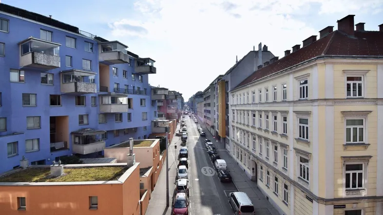 Blick auf eine belebte Stadtstraße mit verschiedenen Wohngebäuden und parkenden Autos.