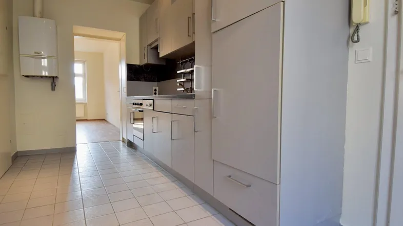 Helle Küche mit weißen Fliesenboden, Einbauküche und Gastherme an der Wand.