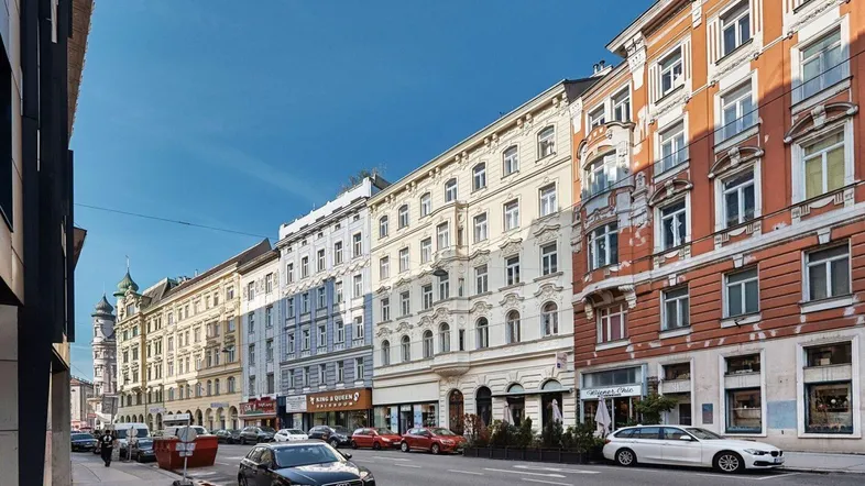 Blick auf eine belebte Stadtstraße mit historischen Gebäuden und parkenden Autos.