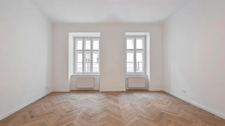 Helles Zimmer mit Fischgrätparkettboden und zwei Fenstern, bereit zur individuellen Gestaltung.