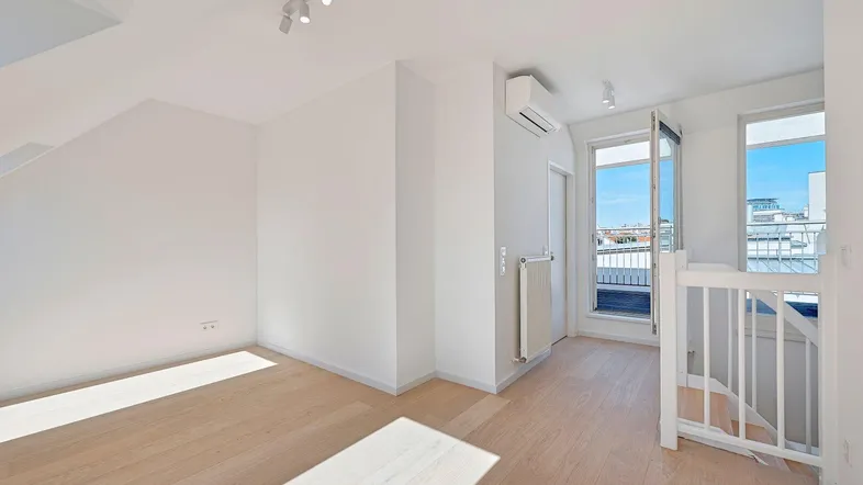 Heller Dachgeschossraum mit Holzboden, Klimaanlage und Zugang zu einem kleinen Balkon.