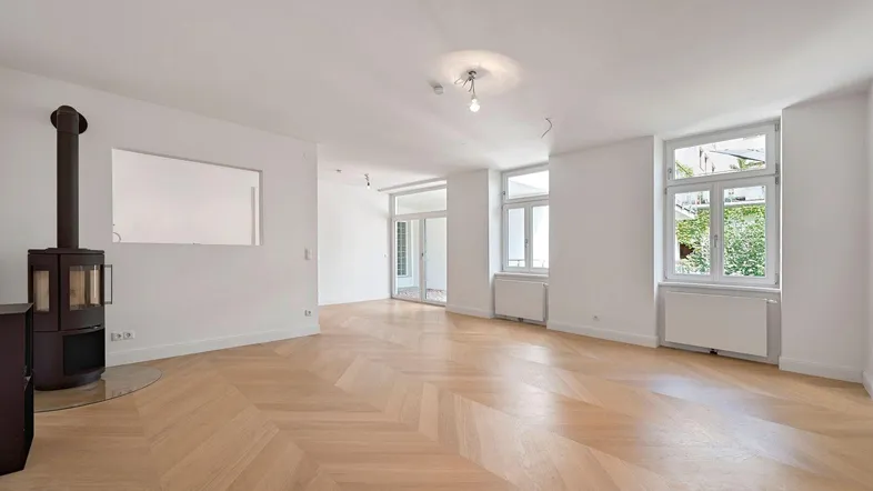 Geräumiges Wohnzimmer mit elegantem Fischgrätparkett, Kaminofen und großen Fenstern.