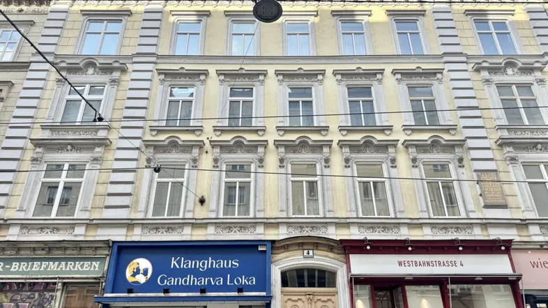 Historische Fassade eines Mehrfamilienhauses mit dekorativen Elementen und Geschäften im Erdgeschoss.