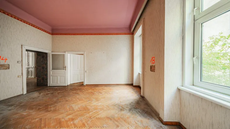Geräumiges Zimmer mit Fischgrätparkett, rosa Decke und großen Fenstern, bereit zur Renovierung.