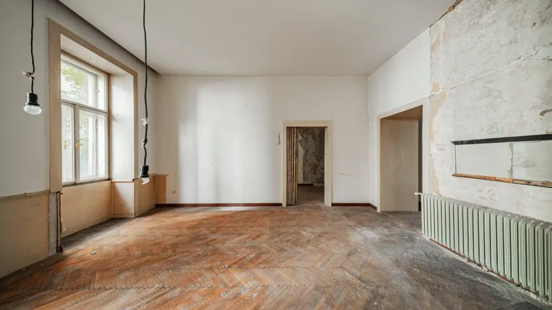 Geräumiger Wohnraum in Renovierung mit Fischgrätparkett, hohen Fenstern und Heizkörper.