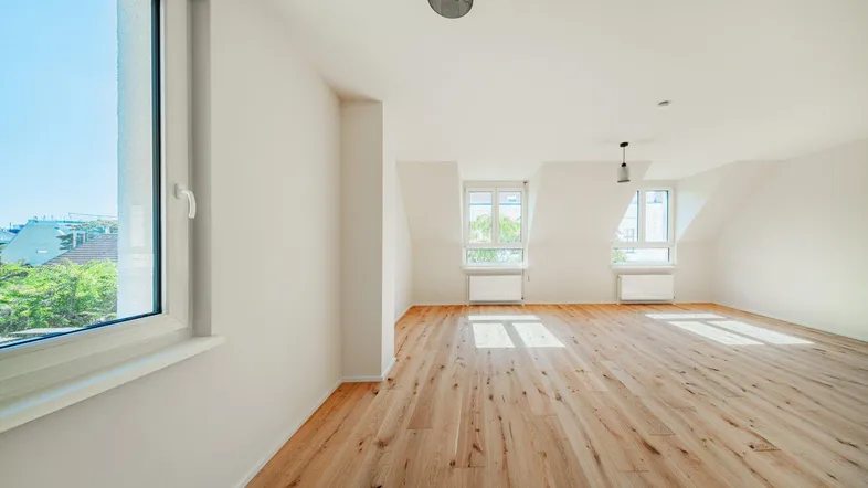 Helles Dachgeschosszimmer mit Holzboden, Dachschrägen und Blick ins Grüne durch große Fenster.