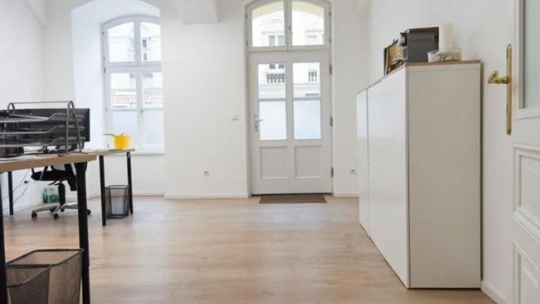 Helles Büro mit hohen Decken, Holzboden und großen, bogenförmigen Fenstern, die viel Tageslicht hereinlassen.